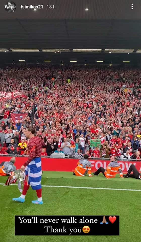 Article image:Kostas Tsimikas thanks Liverpool fans as he poses with a Greek flag and the Carabao Cup in front of the Kop